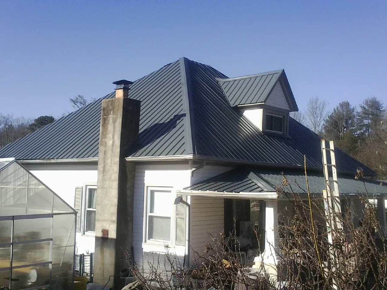 Dark blue standing seam metal roof on a white farmhouse with dormer — Slate & Tile Roof Repair by Roofing Brothers in Powderly