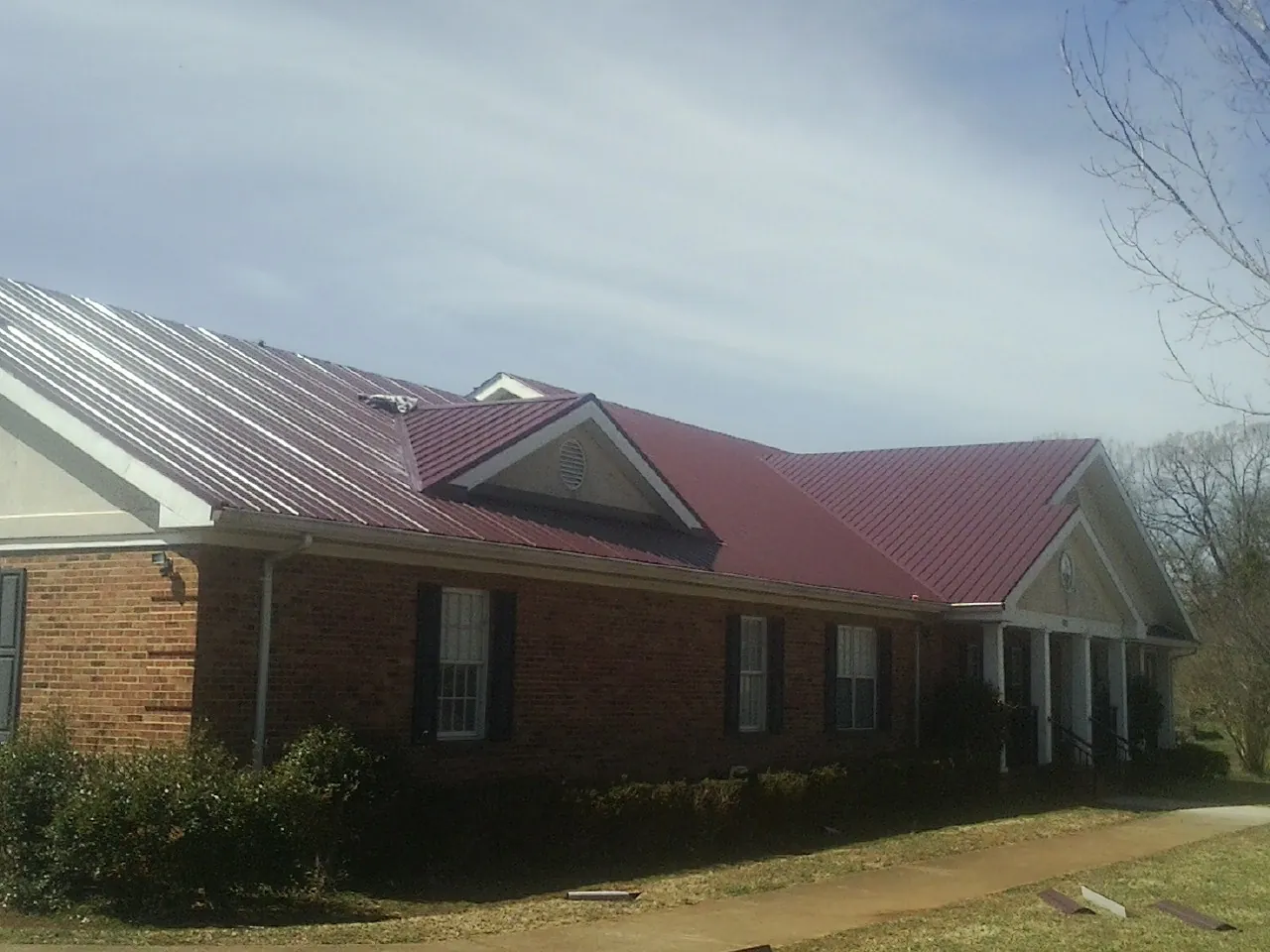 Red metal roof with gabled entries on a long brick building, from a Hail Damage Roof Repair job in Powderly