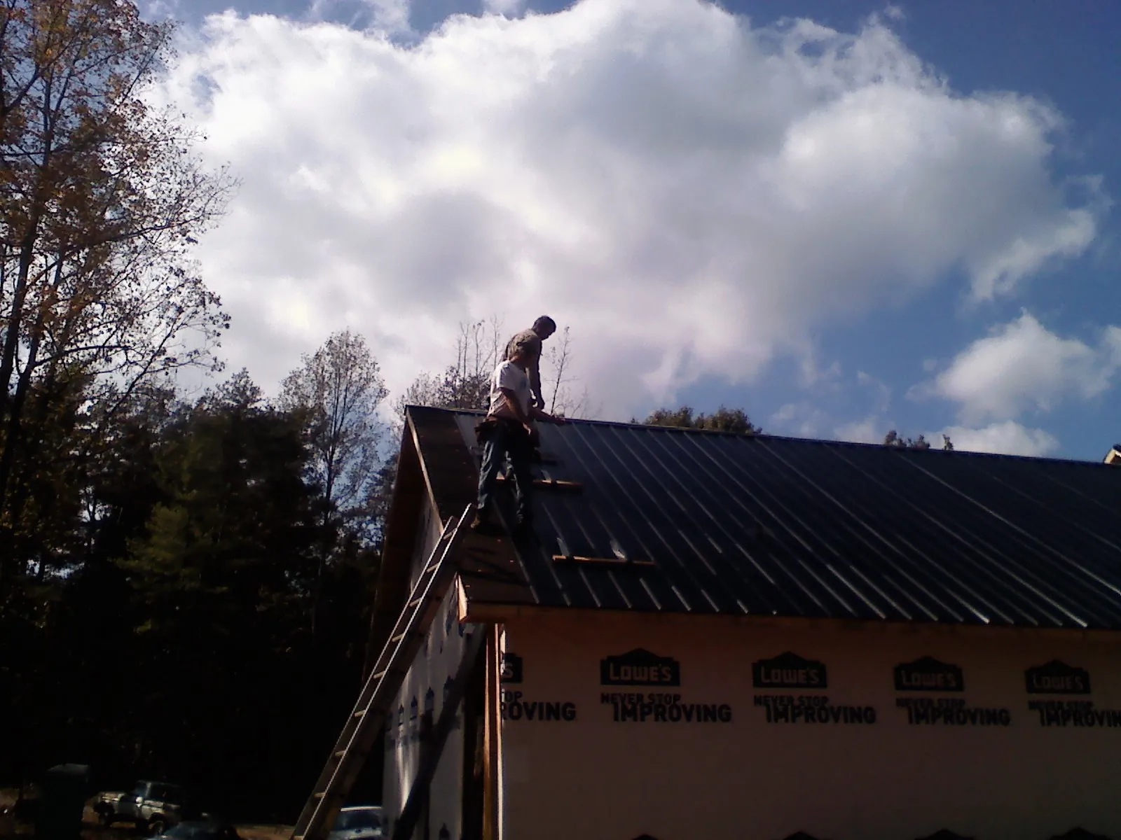 Roofer fastening dark metal panels high against a cloudy sky, from a Roof Inspection job in Powderly