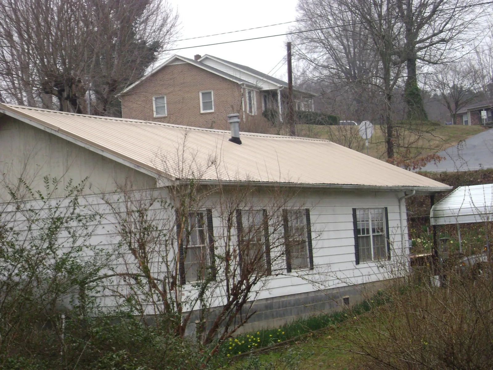 Tan metal roof on a white sided house set into a hillside — Commercial Roofing by Roofing Brothers in Powderly