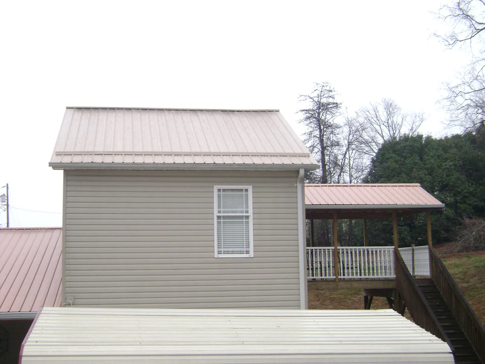 Tan metal roofs on a two story addition and attached porch, from a Roof Replacement job in Powderly